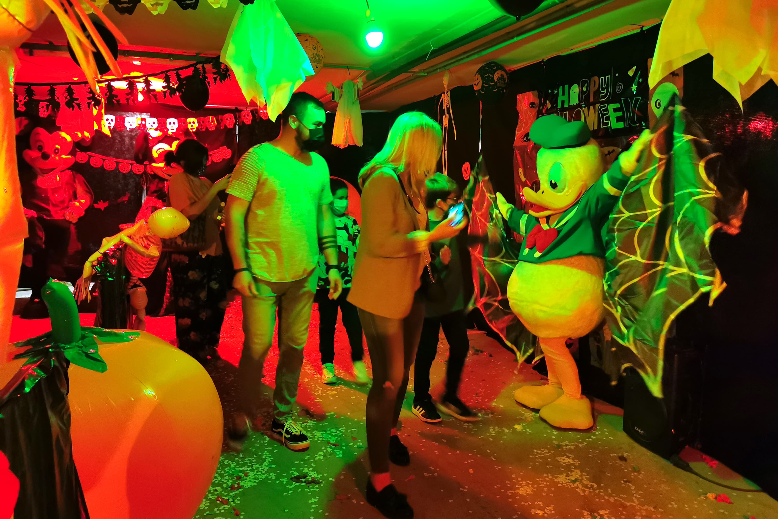 Fiesta disco con mascota Pato Donald Halloween, familias bailando, decoración luces neón