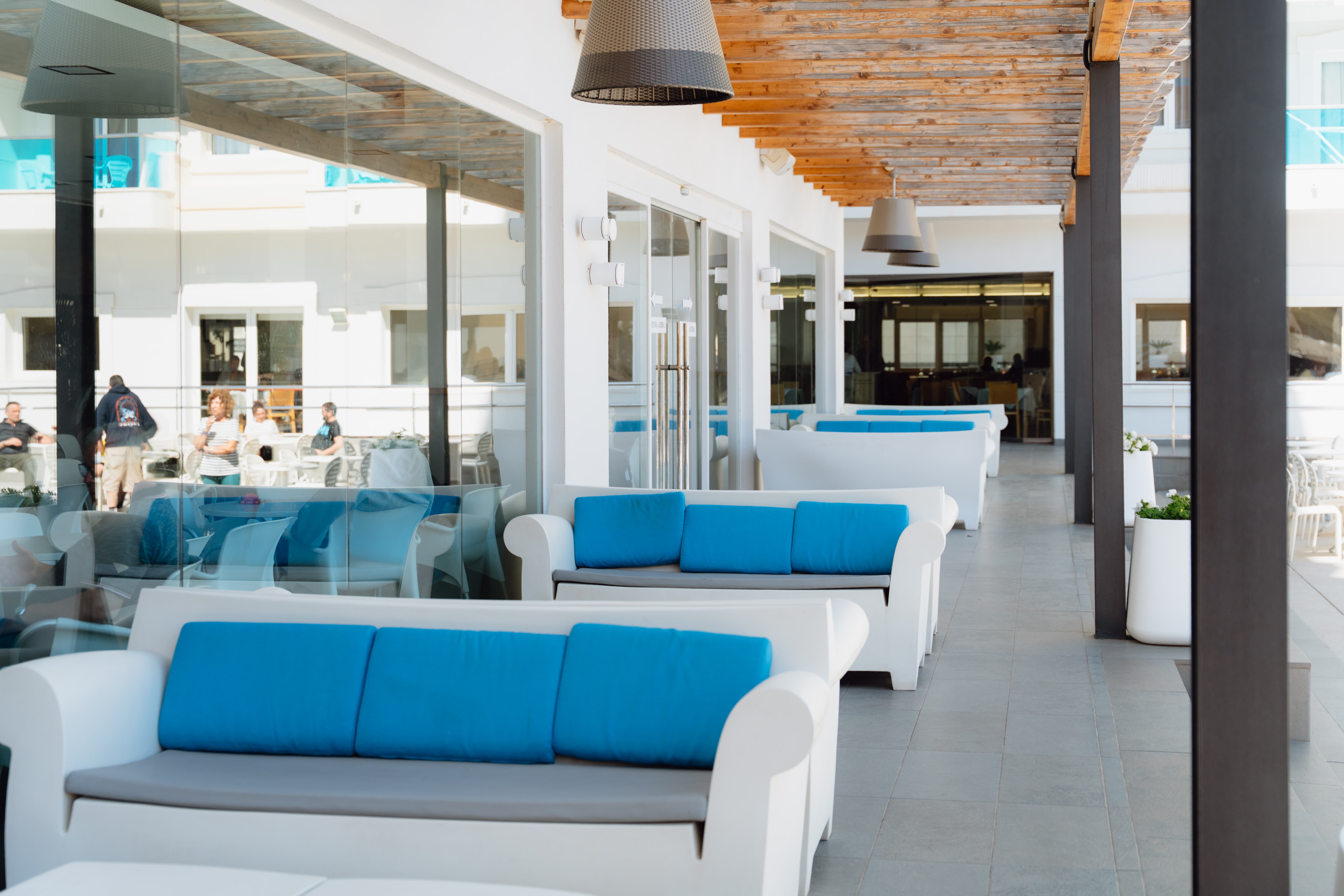 Zona lounge con sofás blancos y cojines azules junto a la piscina del Hotel Acuazul de Peñíscola
